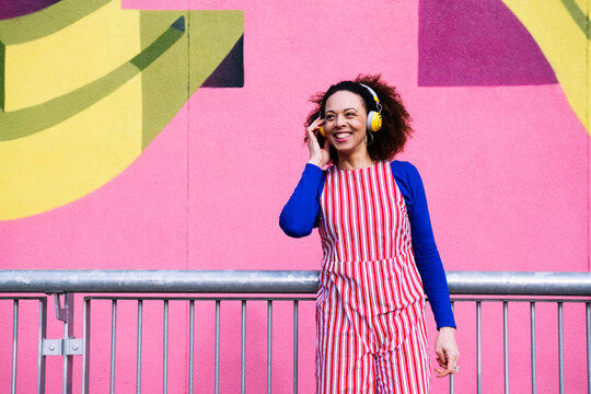 Smiling woman wearing headphones standing in front of pink wall