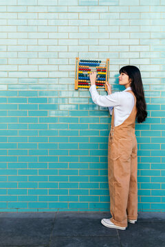Young woman holding abacus on turquoise brick wall