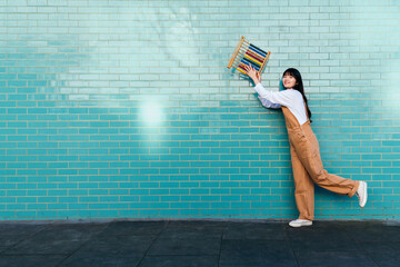 Smiling young woman holding abacus in front of turquoise brick wall