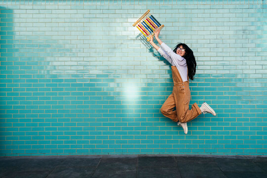 Excited woman jumping with abacus toy in front of turquoise wall