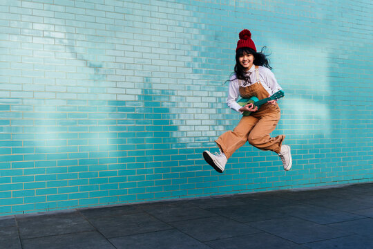 Excited woman playing ukulele and jumping on footpath