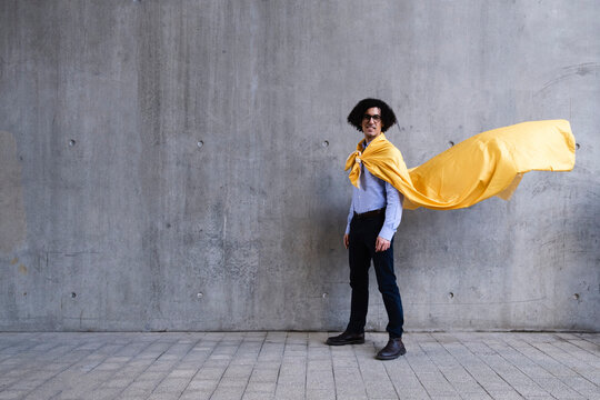 Smiling man wearing yellow cape standing in front of gray wall