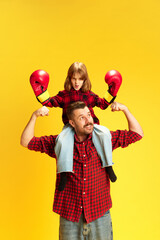 Fototapeta na wymiar Little girl and her father grimacing and demonstrated his power sitting on dad's shoulder against vivid yellow background. Concept of International Day of Happiness, childhood and parenthood. Ad