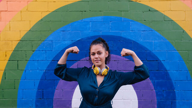 Smiling young woman flexing muscles in front of rainbow wall