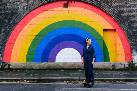 Woman wearing wireless headphones and roller skates in front of rainbow wall