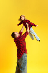 Have fun together. Man lifting laughing child in air imitating airplane against vivid yellow background. Concept of International Day of Happiness, childhood and parenthood, positive emotions. Ad