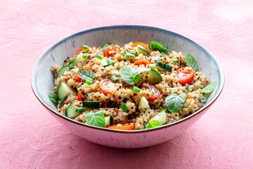 Quinoa tabbouleh salad in a bowl, a healthy dinner with tomatoes and mint, on a pink background