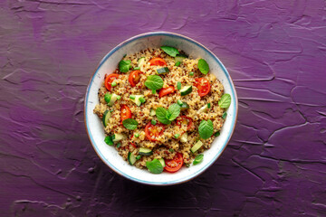 Quinoa tabbouleh salad in a bowl, a healthy dinner with tomatoes and mint, overhead shot on a purple background