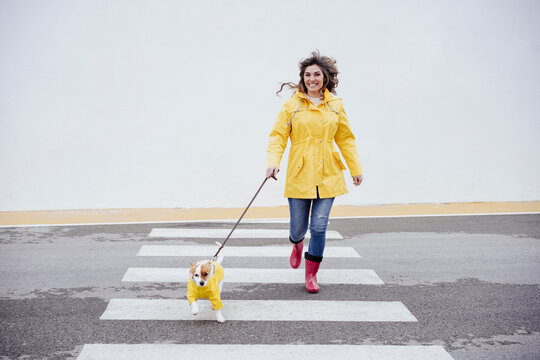 Happy woman running with dog on crosswalk
