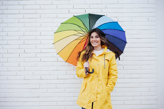 Smiling woman holding multi colored umbrella in front of brick wall