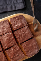 Chocolate brownie, simple coffee cake, overhead flat lay view on a wooden cutting board with a fork