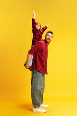 Family. Full length portrait of dad holds on back lovely daughter who very happy because have time with father against vivid yellow background. Concept of International Day of Happiness, childhood. Ad - obrazy, fototapety, plakaty
