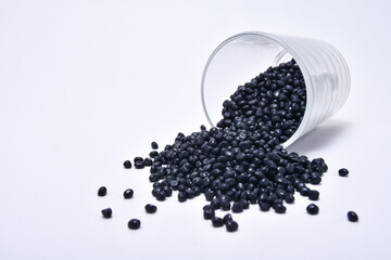 black masterbatch granules spilled from a shot glass and isolated on a white background, this...
