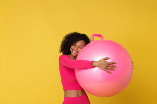 Smiling woman embracing pink ball against yellow background