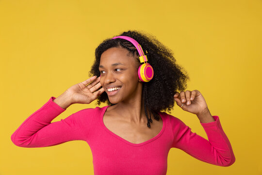 Smiling young woman listening music through wireless headphones against yellow back ground