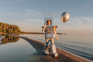 Boy in astronaut suit holding silver balloon at beach