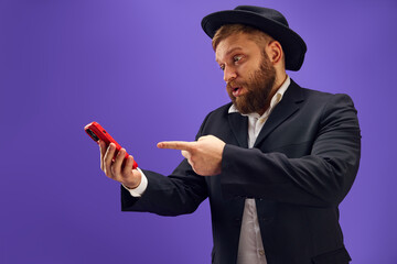 Bearded young Jewish man emotionally looking on mobile phone screen, reading news and messages...