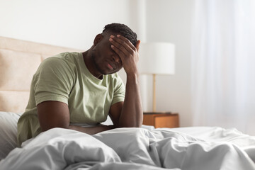 Sleepy tired black man in bed covering face with hand
