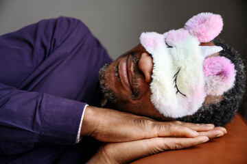 Mature man wearing unicorn eye mask sleeping on bed