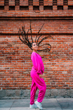 Smiling woman with dreadlocks standing in front of brick wall