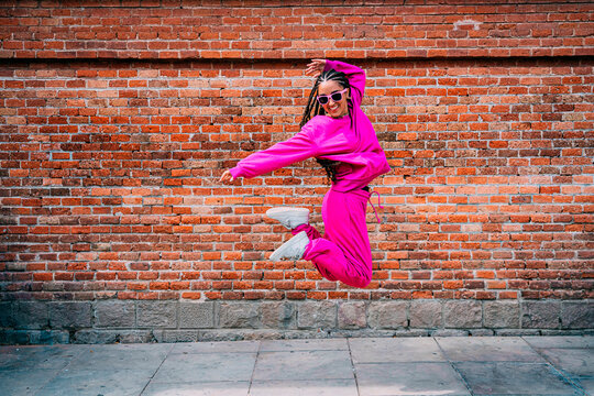Cheerful woman jumping in front of brick wall