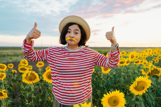 Woman with petals mustache gesturing thumbs up in sunflower field