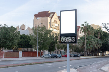 Urban digital clock post with a blank advertising panel against a cityscape, ideal for promotions. Vertical billboard mockup, empty display. Copy space for text, picture.