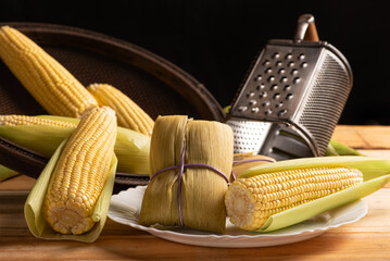 Pamonha and green corn, Pamonha on a white plate and beautiful ears of green corn on rustic wood,...
