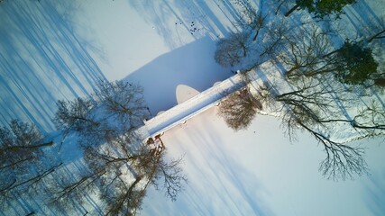 Aerial view of the bridge in the park, frozen pond, long shadow of trees, beautiful winter scenery.
