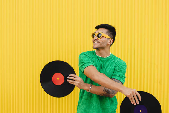 Happy young man having fun with vinyl records in front of wall