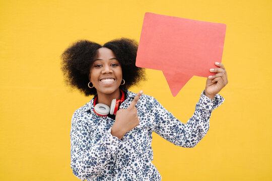 Young woman pointing at speech bubble against yellow wall