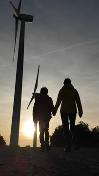 Mother with son walk through a renewable energy wind farm during the sunset. Silhouette of people and wind turbine. Concept sustainability, climate change, saving the earth. green energy and zero emis