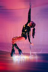 A girl with a beautiful, athletic figure dances on a pole in the light of New Year's lights.