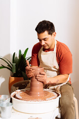 Male potter sitting in a stool working with clay in workshop