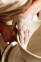 Crop potter hands shaping clay pot on wheel