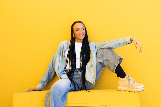 Happy woman wearing denim clothing and sitting near yellow wall