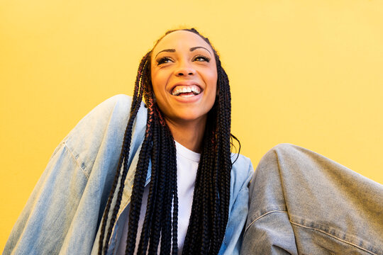 Cheerful woman with braided hair in front of yellow wall