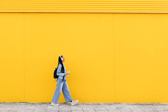 Young woman walking on footpath in front of yellow wall