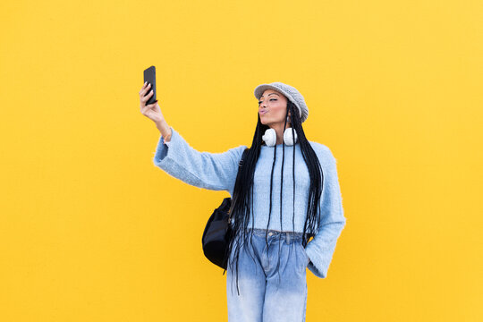 Young woman taking selfie with smart phone in front of yellow wall