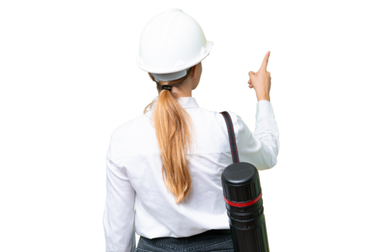 Young architect caucasian woman with helmet and holding blueprints over isolated background pointing back with the index finger