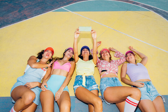 Happy woman with friends watching mobile phone lying on sports court