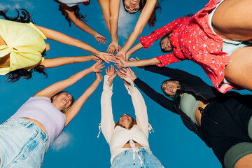 Happy friends with arms raised under blue sky at dusk