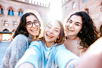 Three smiling young hipster women visit landmarks on vacation in Italy - Happy girls taking selfie...