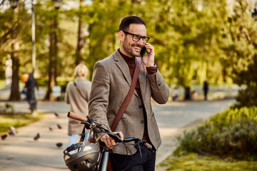A smiling businessman having a phone call while leaning on his bicycle.