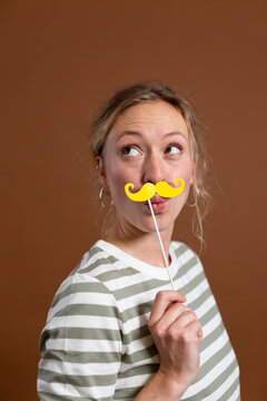Blond woman puckering and holding mustache prop in studio