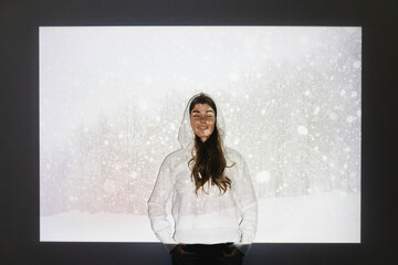 Happy woman with eyes closed standing in front of snowfall on projection screen