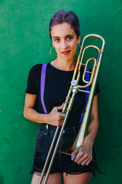Smiling woman holding trombone in front of wall
