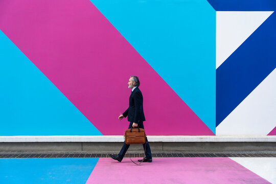 Businessman with bag walking in front of multi colored wall