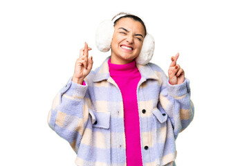Young woman wearing winter muffs over isolated chroma key background with fingers crossing