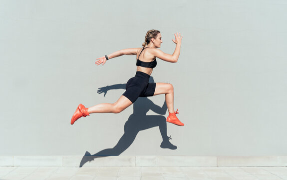 Young woman jumping by gray wall